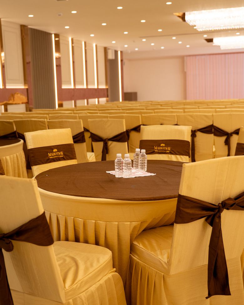Round banquet tables in gold covers with Mahotsav chair sashes, facing a stage